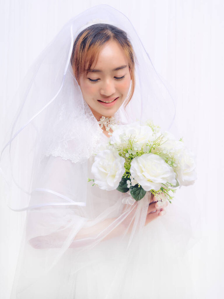 studio portrait of asian bride in white gown with veil holding flower bouquet on white background - Fotografie, Obrázek