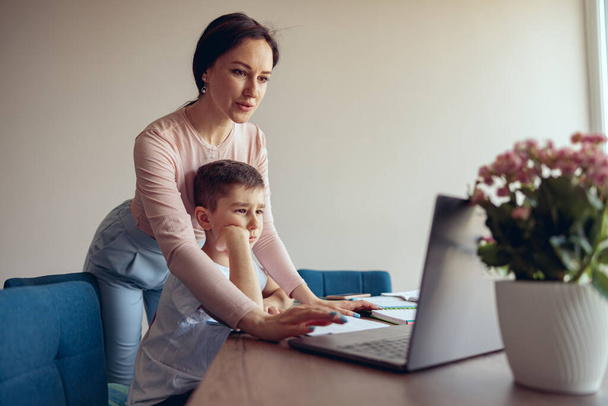 Красива молода мати допомагає маленькому синові вчитися онлайн в ноутбуці. Домашня освіта
. - Фото, зображення