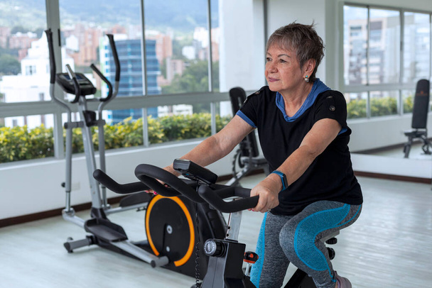 Mujer latina mayor hace ejercicio en el gimnasio usando las máquinas de entrenamiento - Foto, Imagen