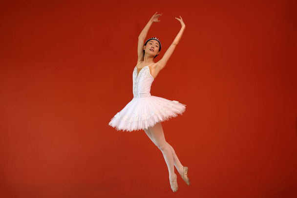 Beautiful Asian woman ballet dancer practice dance jump move wearing tutu at home red orange background wall - Photo, Image