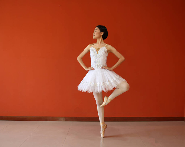 Beautiful Asian woman ballet dancer practice dance jump move wearing tutu at home red orange background wall - Photo, Image
