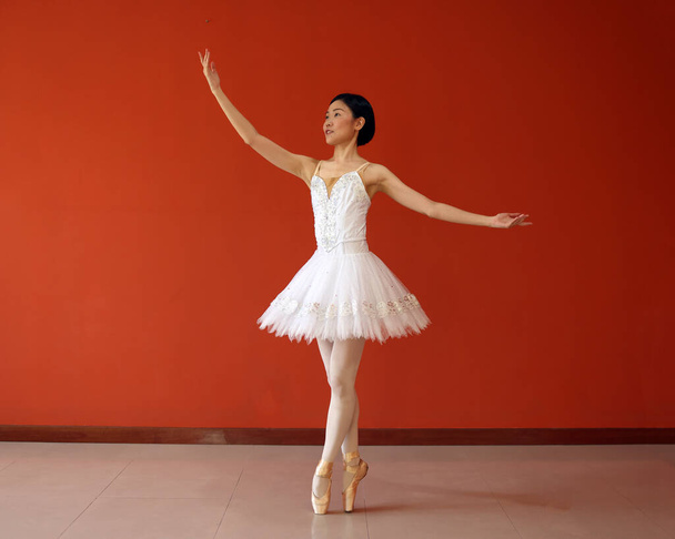 Gyönyörű ázsiai nő balett táncos gyakorlat tánc ugrás mozog visel tutu otthon piros narancs háttér fal - Fotó, kép