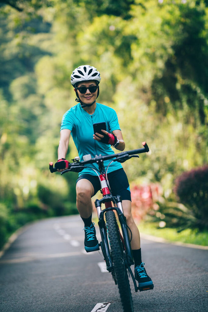 Woman using smart phone cycling on tropical park trail in summer - Фото, зображення