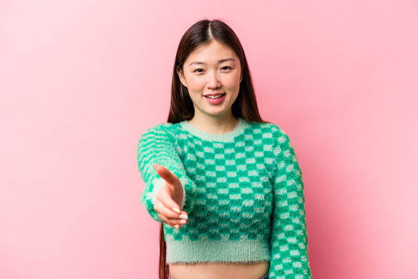 Молодая китаянка на розовом фоне протягивает руку к камере в приветственном жесте. - Фото, изображение