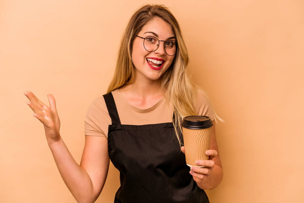Restaurantkellner kaukasische Frau mit einem Kaffee zum Mitnehmen isoliert auf beigem Hintergrund erhalten eine angenehme Überraschung, aufgeregt und hebt die Hände. - Foto, Bild