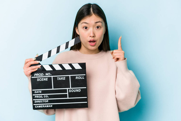 Nuori aasialainen nainen tilalla clapperboard eristetty sinisellä pohjalla ottaa joitakin hyviä ideoita, käsite luovuutta. - Valokuva, kuva