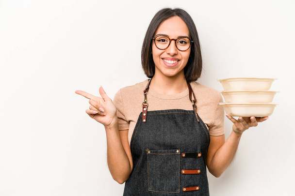 Young caucasian waitress woman holding tupperware isolated on white background smiling and pointing aside, showing something at blank space. - Photo, Image