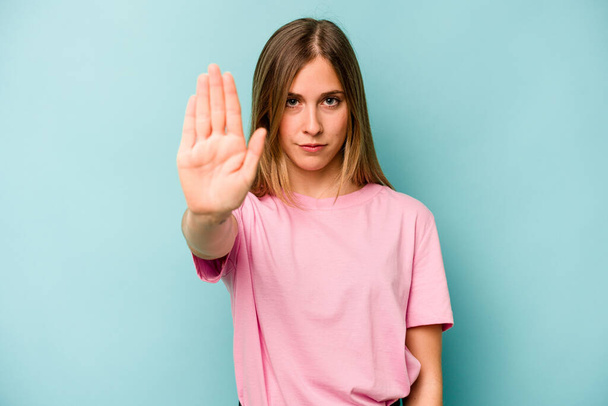 Young caucasian woman isolated on blue background standing with outstretched hand showing stop sign, preventing you. - Foto, Imagen