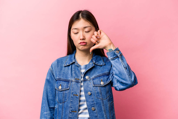 Молодая китаянка, изолированная на розовом фоне, показывает неприязненный жест, опущенные пальцы. Концепция разногласий. - Фото, изображение
