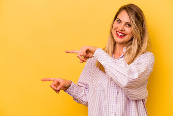 Young caucasian woman isolated on yellow background pointing with forefingers to a copy space, expressing excitement and desire. - Photo, Image