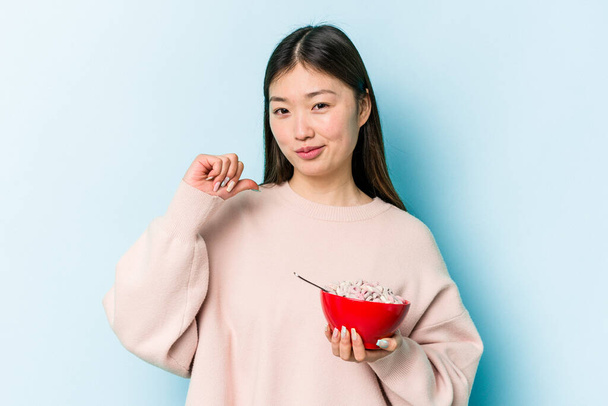 Fiatal ázsiai nő kezében egy tál gabonafélék elszigetelt kék háttér úgy érzi, büszke és magabiztos, példa, hogy kövesse. - Fotó, kép