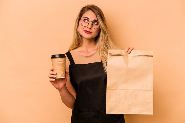Restaurante camarero caucásico mujer sosteniendo un llevar café y bolsa aislado sobre fondo beige - Foto, imagen