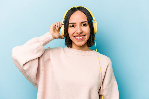 Fiatal spanyol nő hallgat zenét elszigetelt kék háttér - Fotó, kép