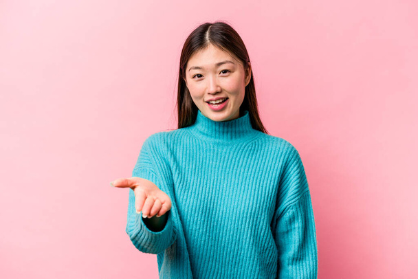 Young Chinese woman isolated on pink background stretching hand at camera in greeting gesture. - Foto, afbeelding