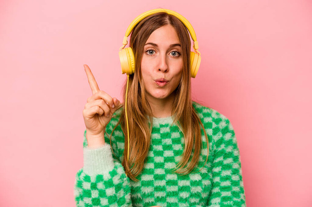 Young caucasian woman listening to music isolated on pink background having some great idea, concept of creativity. - Photo, Image