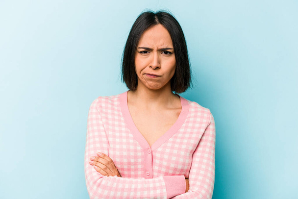 Young hispanic woman isolated on blue background frowning face in displeasure, keeps arms folded. - Φωτογραφία, εικόνα
