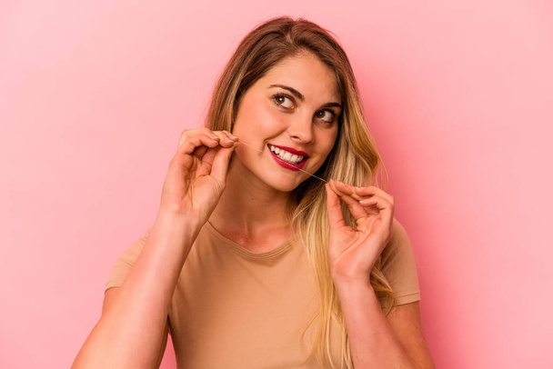 Young caucasian woman holding dental floss isolated on pink background - Фото, зображення