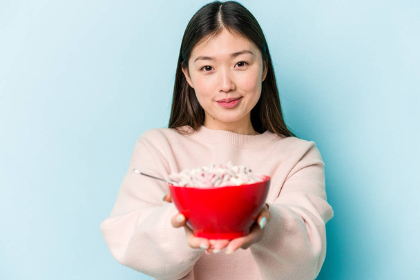Joven asiática sosteniendo un bowl de cereales aislado sobre fondo azul - Foto, imagen