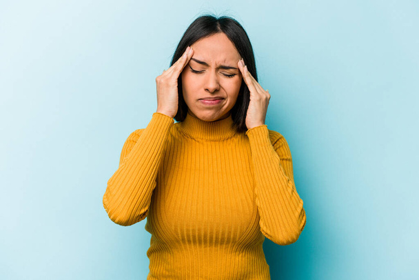 Junge hispanische Frau isoliert auf blauem Hintergrund mit Kopfschmerzen, Berührung vor dem Gesicht. - Foto, Bild