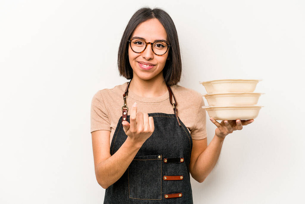 Young caucasian waitress woman holding tupperware isolated on white background pointing with finger at you as if inviting come closer. - Photo, Image