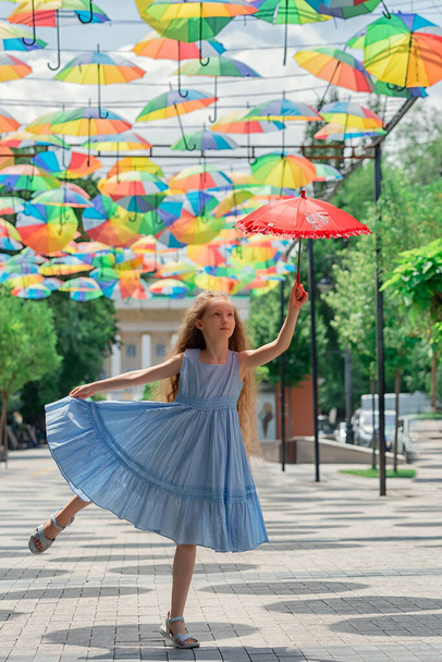 Pretty kid girl jumping while holding a red umbrella. Beautiful child flying - Фото, изображение
