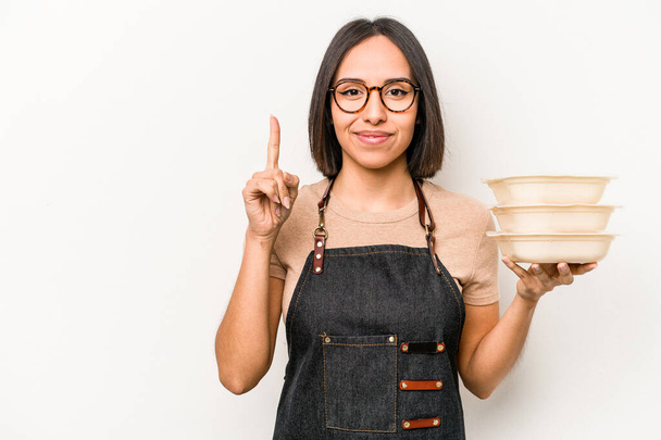 Young caucasian waitress woman holding tupperware isolated on white background showing number one with finger. - Photo, Image