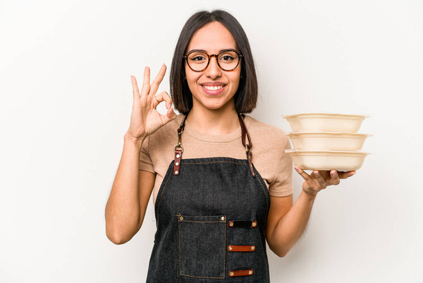 Молодая кавказская официантка, держащая в руках посуду, изолированную на белом фоне, веселая и уверенная в себе, демонстрирующая нормальный жест. - Фото, изображение