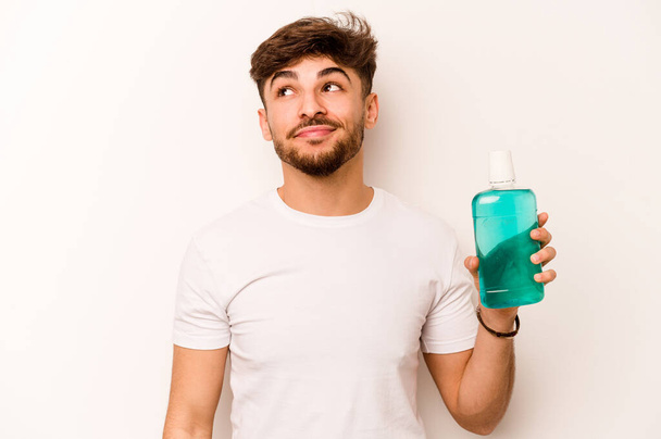 Young hispanic man holding mouthwash isolated on white background dreaming of achieving goals and purposes - Foto, immagini