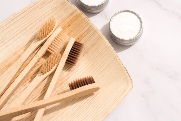 Bamboo toothbrushes and mineral toothpowder, kaolin in aluminium containers over white table background. Natural bath products, organic dentifrice. Mockup image. Top view - Fotoğraf, Görsel