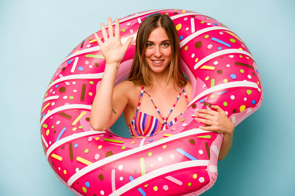 Young caucasian woman holding air mattress isolated on blue background smiling cheerful showing number five with fingers. - Foto, immagini