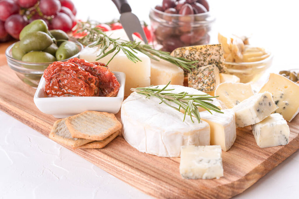 Charcuterie sajt fórumon különféle sajtok szolgált olajbogyó, napon szárított paradicsom és gyógynövények fehér asztal háttér. Sajtlemez aperitifnek - brie, dorblu, gorgonzola, camembert és parmezán - Fotó, kép