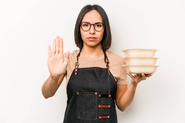Young caucasian waitress woman holding tupperware isolated on white background standing with outstretched hand showing stop sign, preventing you. - Photo, Image