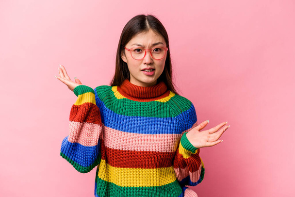 Young Chinese woman isolated on pink background confused and doubtful shrugging shoulders to hold a copy space. - Photo, Image
