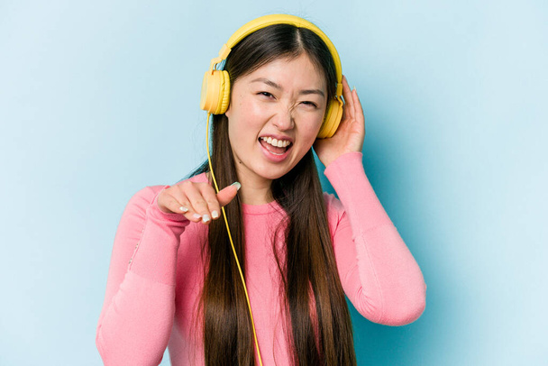 Young asian woman listening to music isolated on blue background - Zdjęcie, obraz