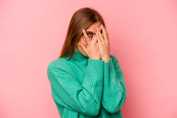 Young caucasian woman isolated on pink background blink through fingers frightened and nervous. - Photo, Image