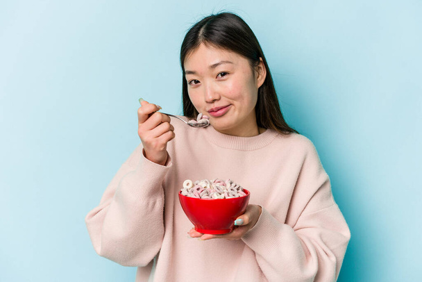 Молодая азиатская женщина держит миску зерновых изолированных на синем фоне - Фото, изображение