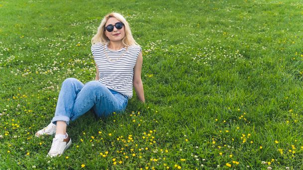 plan complet d'une jolie fille blonde assise sur l'herbe verte. Photo de haute qualité - Photo, image