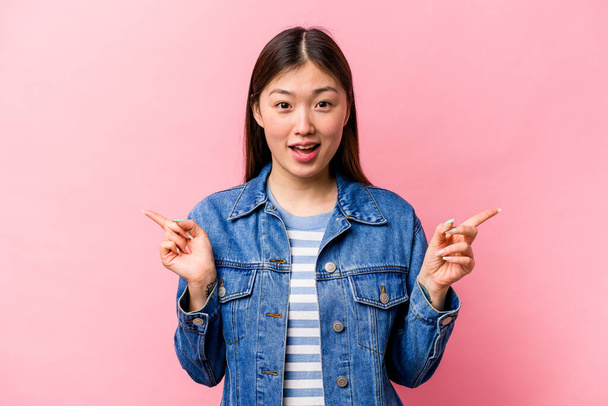 Молодая китаянка выделяется на розовом фоне, указывая на разные места для копирования, выбирая одно из них, показывая пальцем. - Фото, изображение
