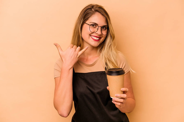Restaurace číšník běloška žena drží odnést kávu izolované na béžové pozadí ukazující mobilní telefon gesto hovoru s prsty. - Fotografie, Obrázek