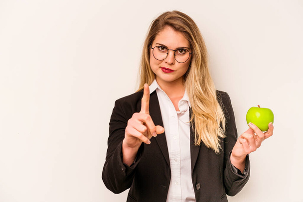 Joven mujer caucásica de negocios sosteniendo una manzana aislada sobre fondo blanco mostrando el número uno con el dedo. - Foto, imagen