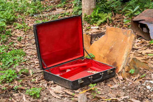 Μια εγκαταλελειμμένη κόκκινη και μαύρη άδεια βαλίτσα στην άγρια φύση - Φωτογραφία, εικόνα