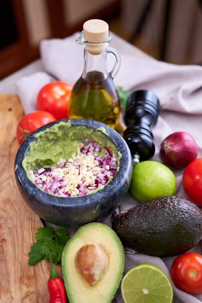 making guacamole - crushed avocado in marble mortar and ingredients. - Foto, Imagem
