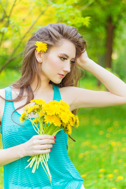 Beautiful girl in a Sunny summer day walking in the garden and keeps yellow dandelions in the hands - Photo, image