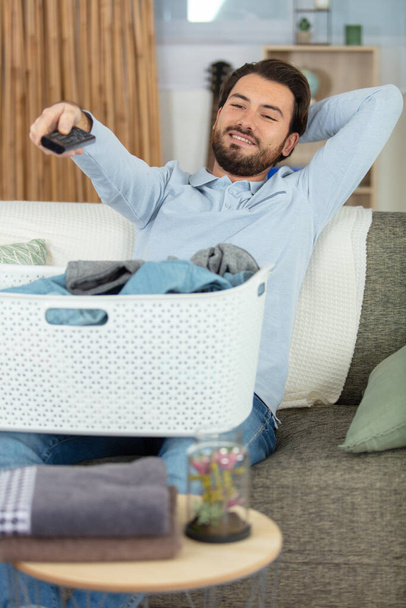 man with laundry basket on his lap watching tv - Fotó, kép