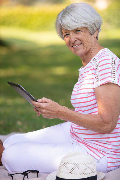 happy senior woman with digital tablet laying on grass - Foto, afbeelding