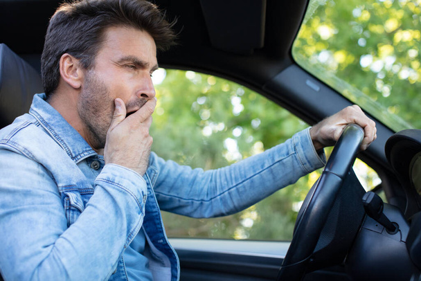 tired man yawning on the front seat of the car - 写真・画像