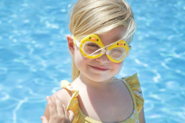 Portrait of toddler girl wearing swimming goggles with clear blue water background - Фото, изображение