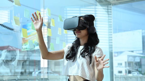 Mladá vývojářka nosí brýle virtuální reality, interagující s digitálním rozhraním v moderní kanceláři. Inovační koncept. - Fotografie, Obrázek