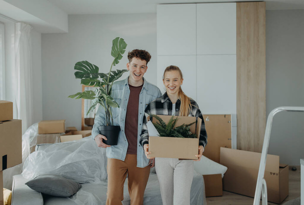 A cheerful young couple in their new apartment, carrying boxes. Conception of moving. - Фото, изображение