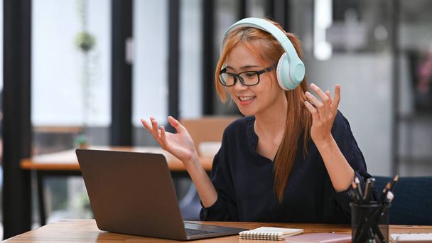 Jonge vrouwelijke werknemer het dragen van een draadloze hoofdtelefoon en kijken naar online webinar op laptop computer. - Foto, afbeelding